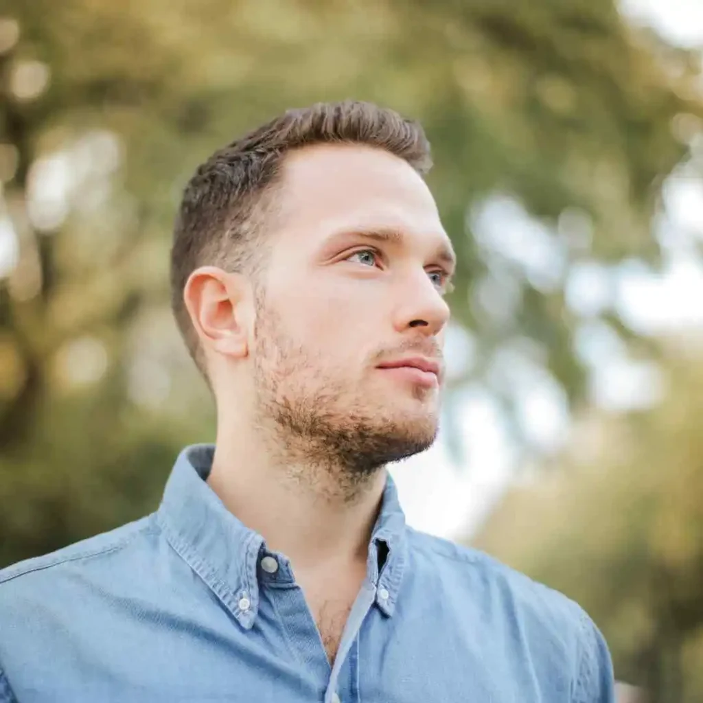 A man in a blue shirt looking off into the distance, showcasing haircuts for men with diamond face.