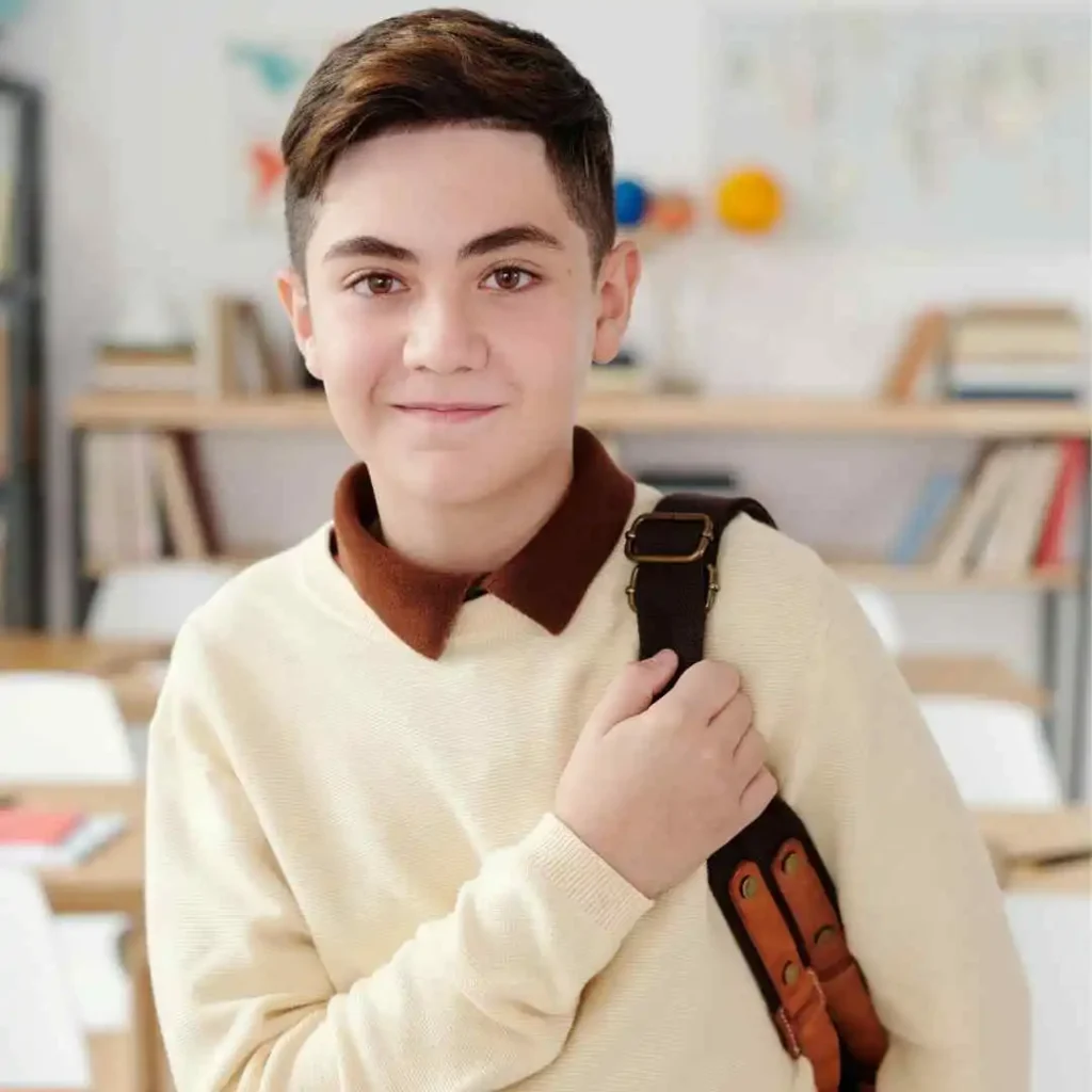 Person in a cream sweater holding a bag strap, with a bookshelf in the background.