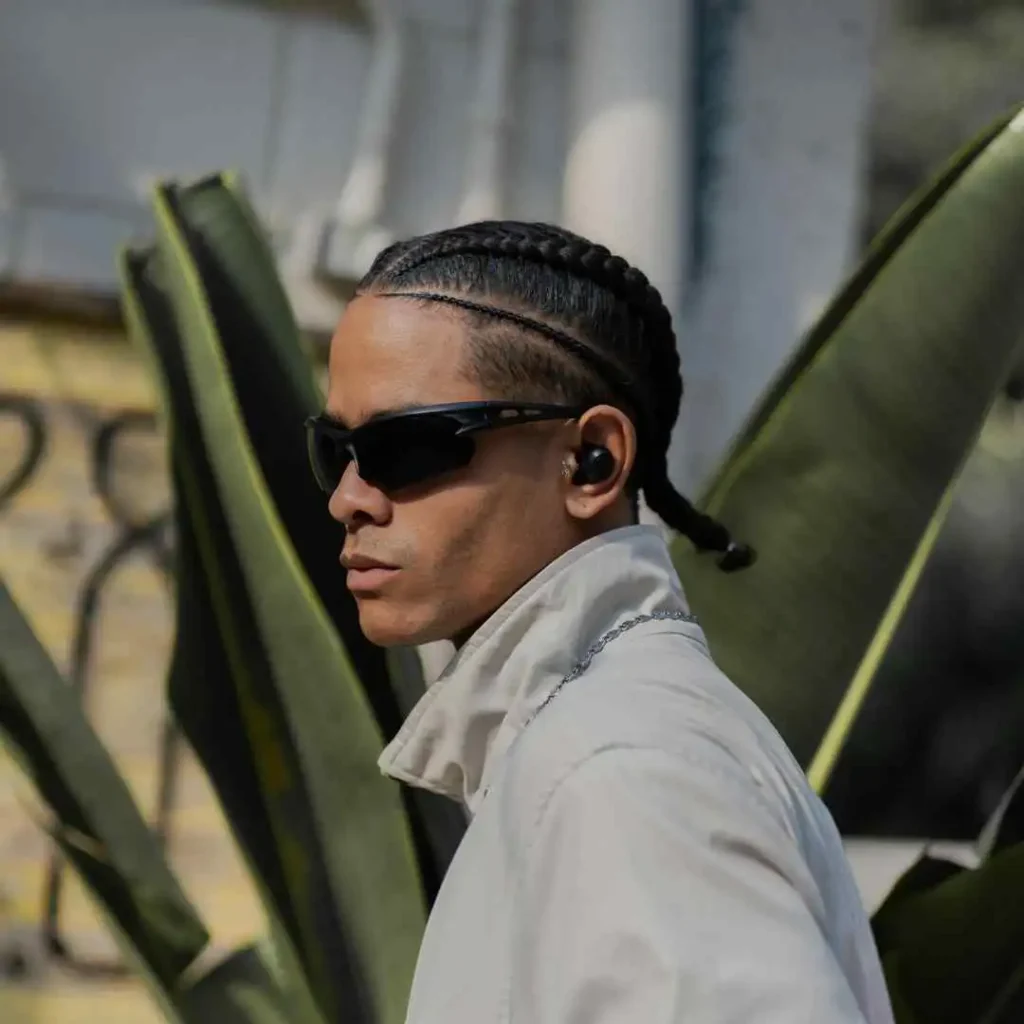 A man with a pair of ear buds in his ears and sporting a pompadour hairstyle.