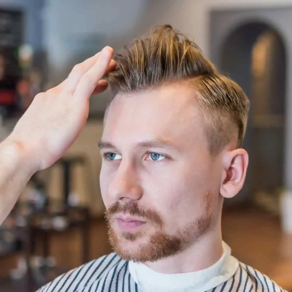 A man getting his hair cut by a barber, with a pompadour hairstyle being shaped.