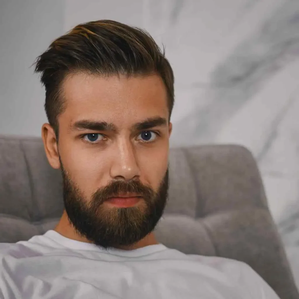 Person with modern hairstyle sitting on a gray sofa, against a marble background.