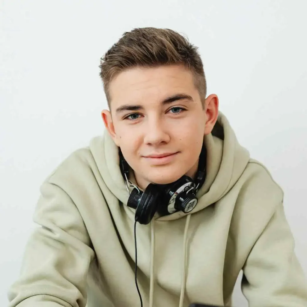 Person with headphones around neck wearing a beige hoodie against a white background.