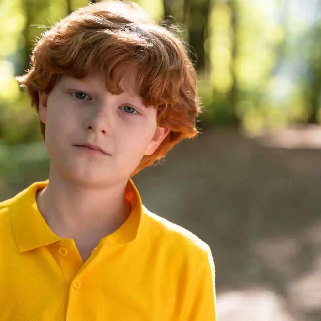 Child in yellow shirt outdoors with trees in the background.