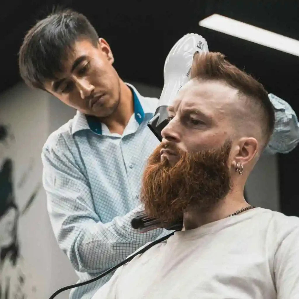 A man getting his hair cut by a barber, focusing on a hairstyle that complements a long face shape. Men hairstyles long face.