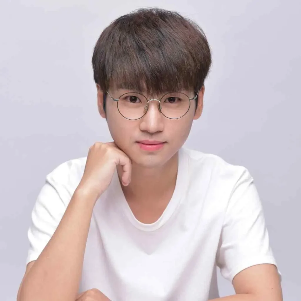 Person in a white T-shirt resting chin on hand, neutral background.