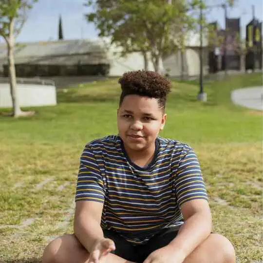 Person in striped shirt sitting on grass with blurred face.