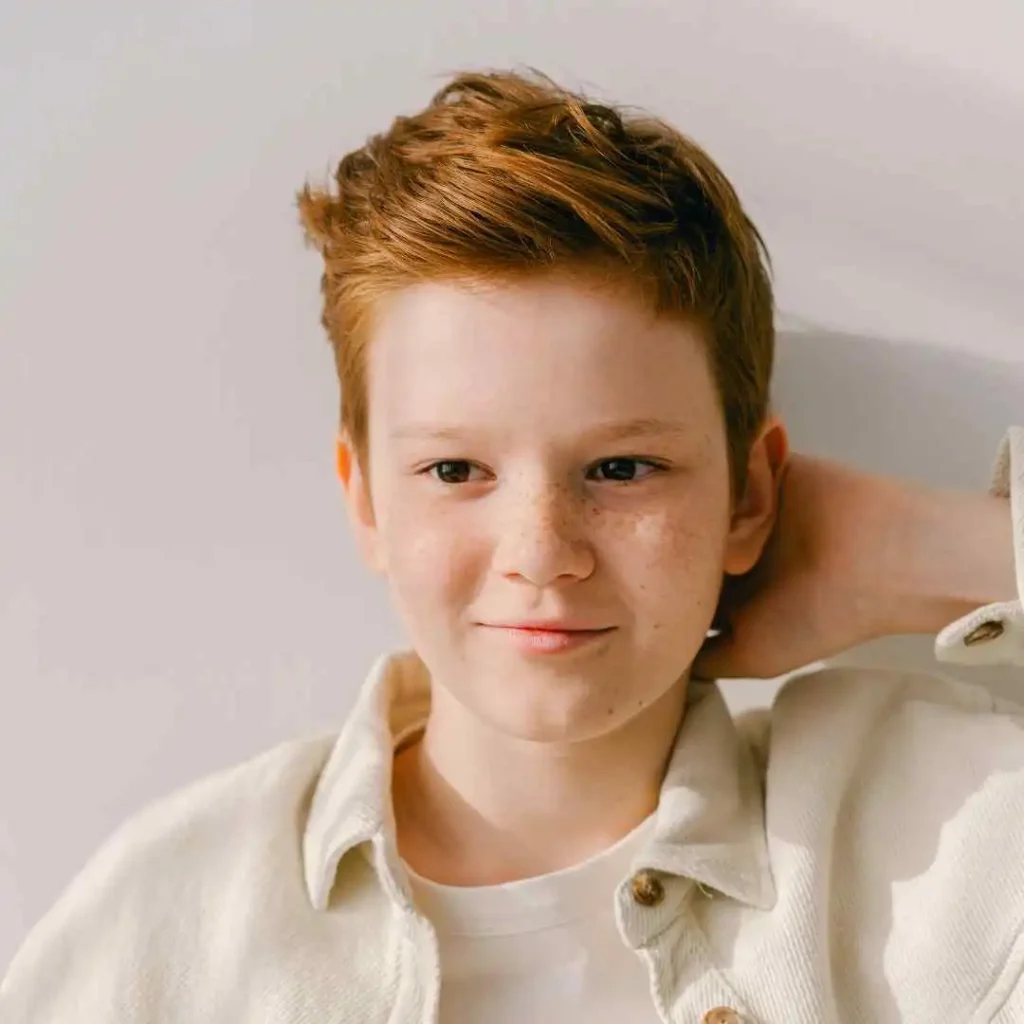 Person in a beige jacket and white shirt against a light background. Teenage boy Haircuts style. 