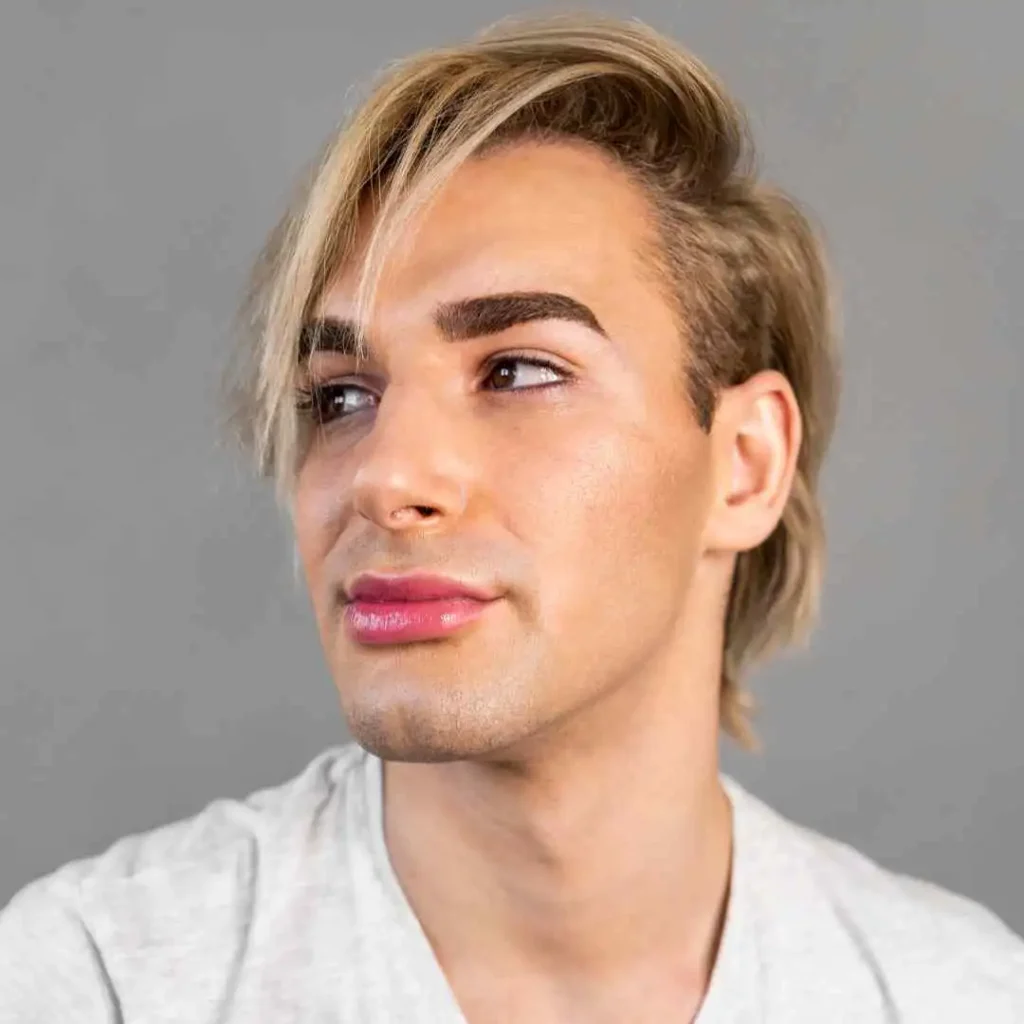 Person with short blond hair wearing a gray t-shirt against a gray background.