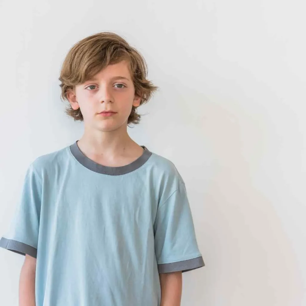 Young individual in light blue t-shirt standing against a white background.