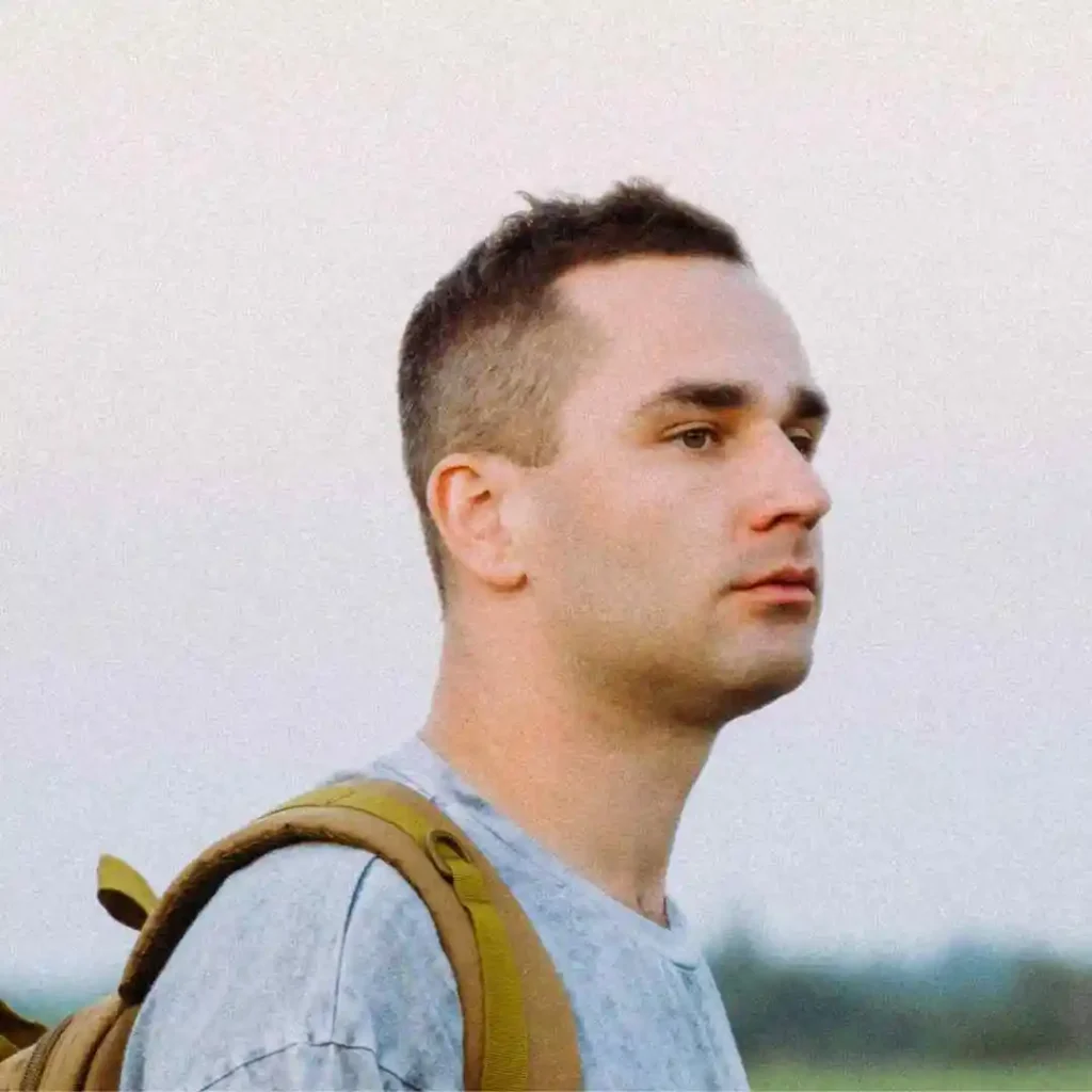 Person in a blue shirt carrying a backpack, with a clear sky in the background.