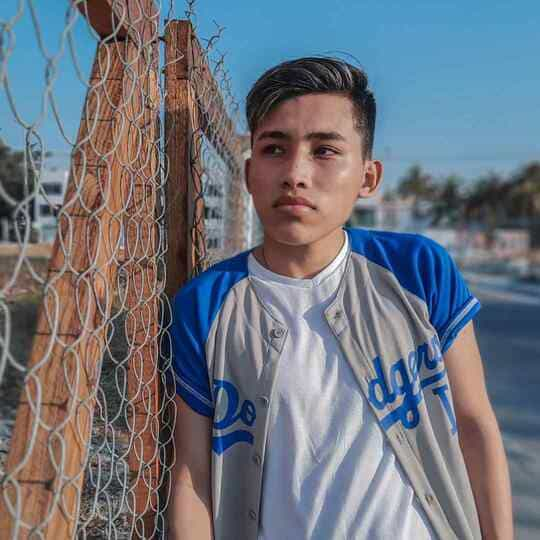 Person in a Dodgers baseball jersey standing by a chain-link fence.