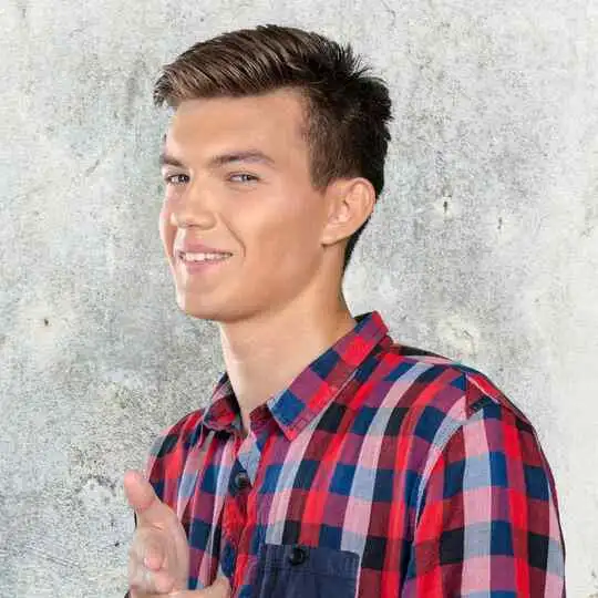 Person in a red and blue plaid shirt standing against a textured wall.