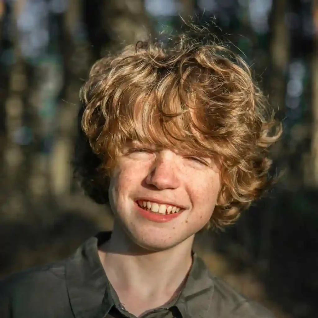 Person with curly hair in a forest setting.