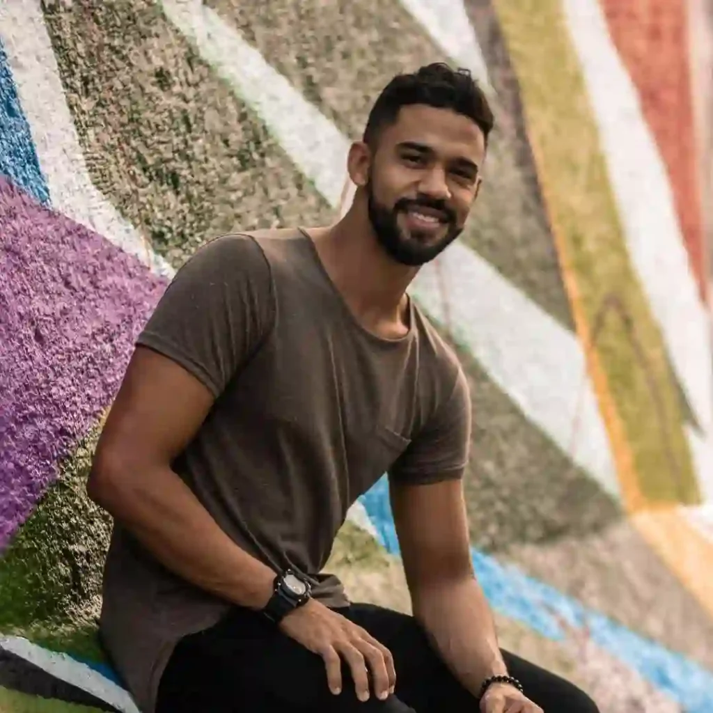 Person in a gray shirt sitting before a colorful graffiti wall.