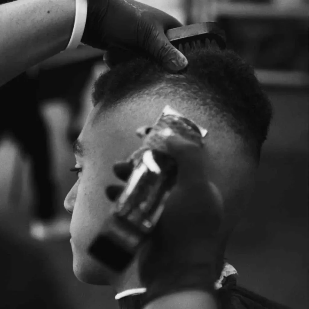 Black and white photo of a person getting a haircut with electric clippers.