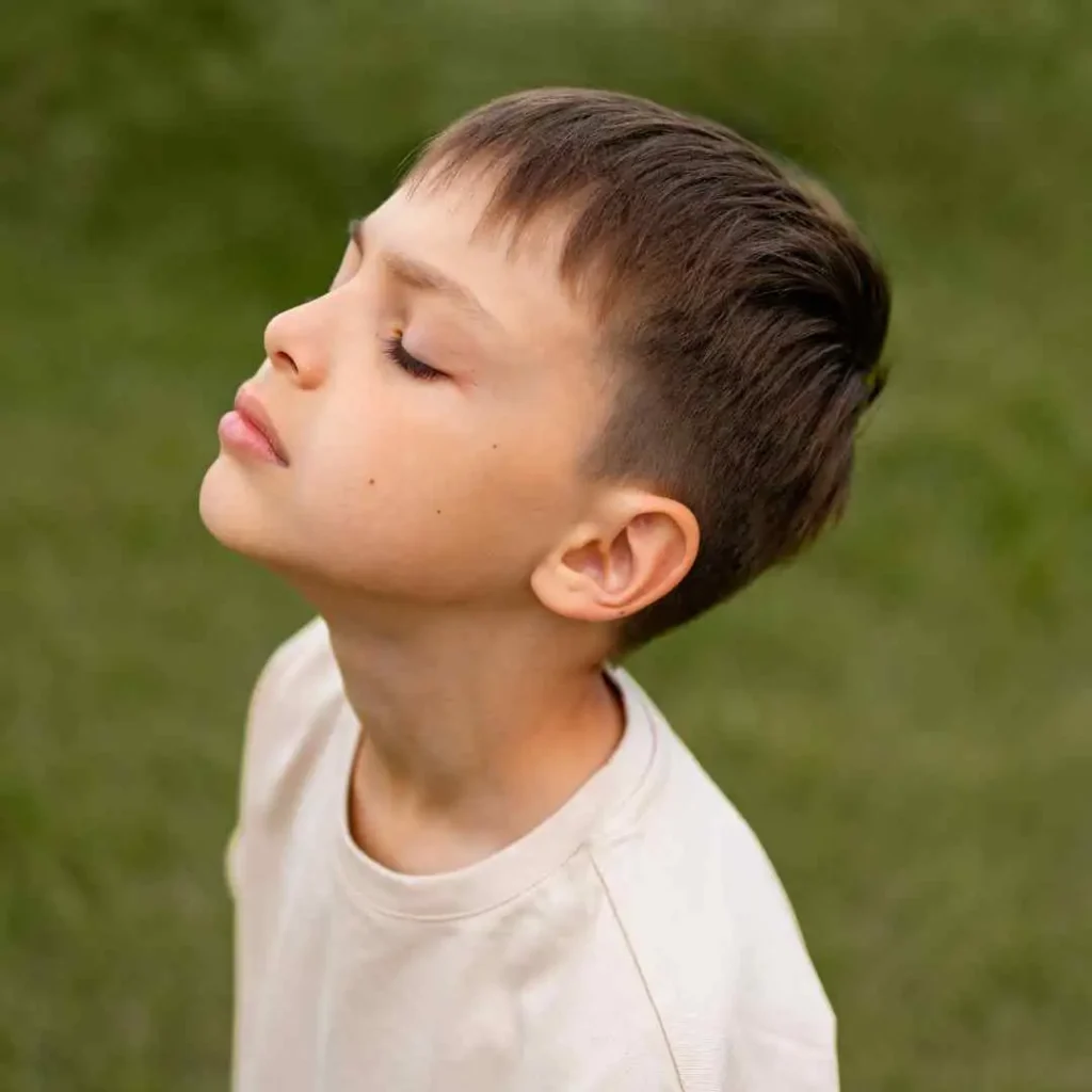 A side view of a child with a neat haircut wearing a white shirt against a green background.