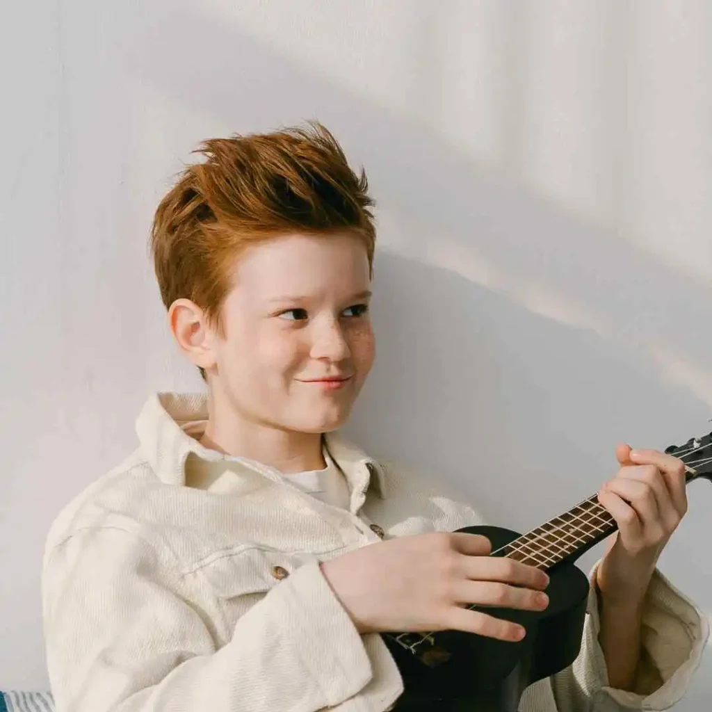 Person in a light jacket playing a ukulele.