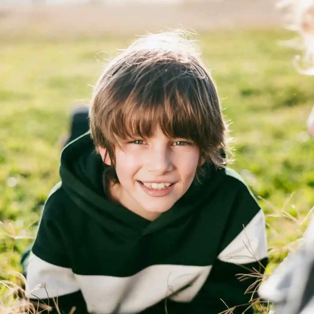 Person in a striped hoodie sitting on grass with sunlight in the background.