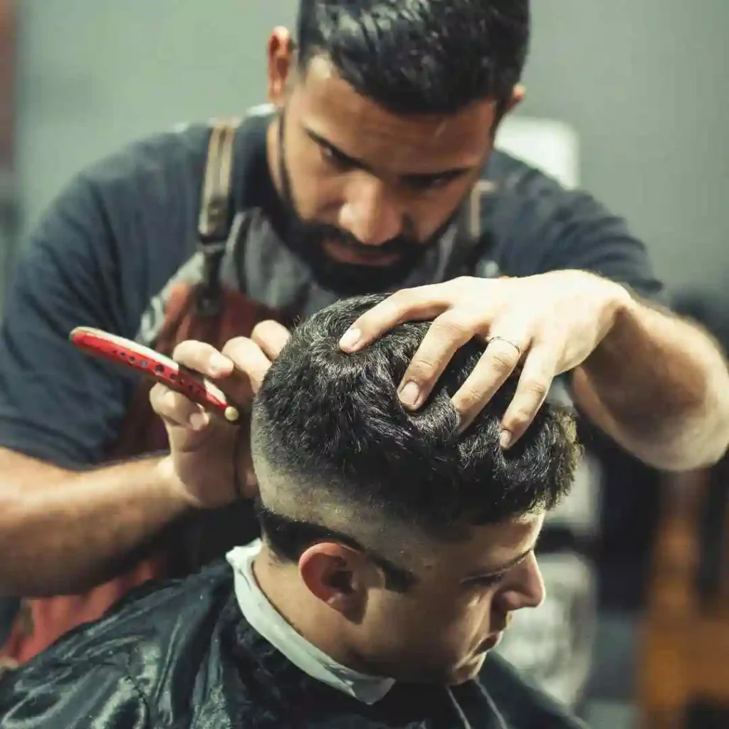 A barber styles a customer's hair with a comb and scissors, focused on creating a precise MEN HAIRSTYLES BUZZ CUT in a modern barbershop setting.