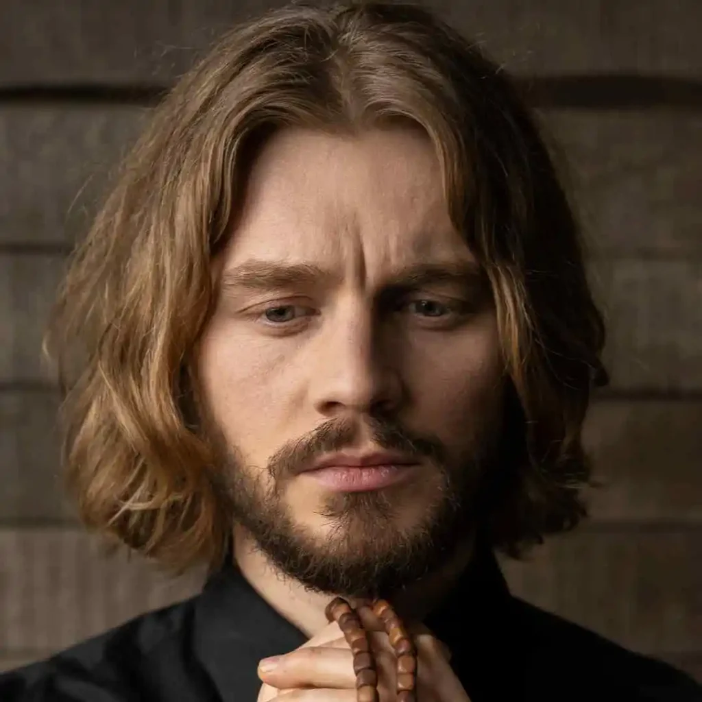 Person with brown hair in black attire, holding prayer beads.