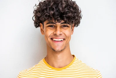 A person showcasing MEN'S SHORT CURLY HAIRCUTS, with curly hair wearing a yellow and white striped shirt, posed neutrally against a plain white background.