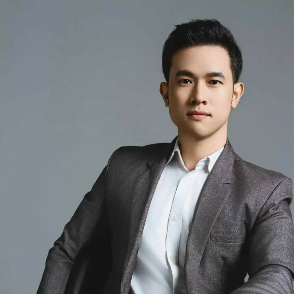 "A person in a dark suit and white shirt showcasing MEN HAIRSTYLES QUIFF poses confidently against a plain gray background, conveying professionalism and poise.