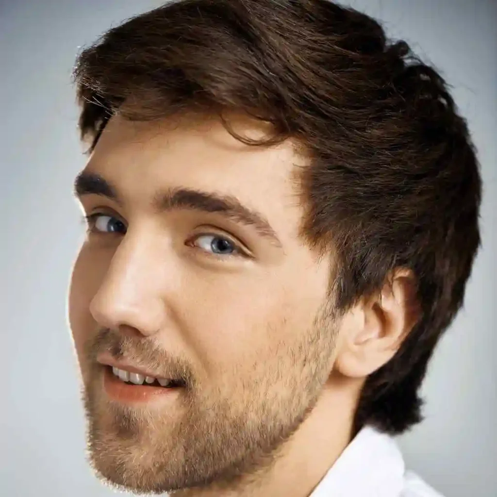 A young man with stylish dark hair showcasing men hairstyles oval face, wearing a white shirt, positioned against a soft grey background.