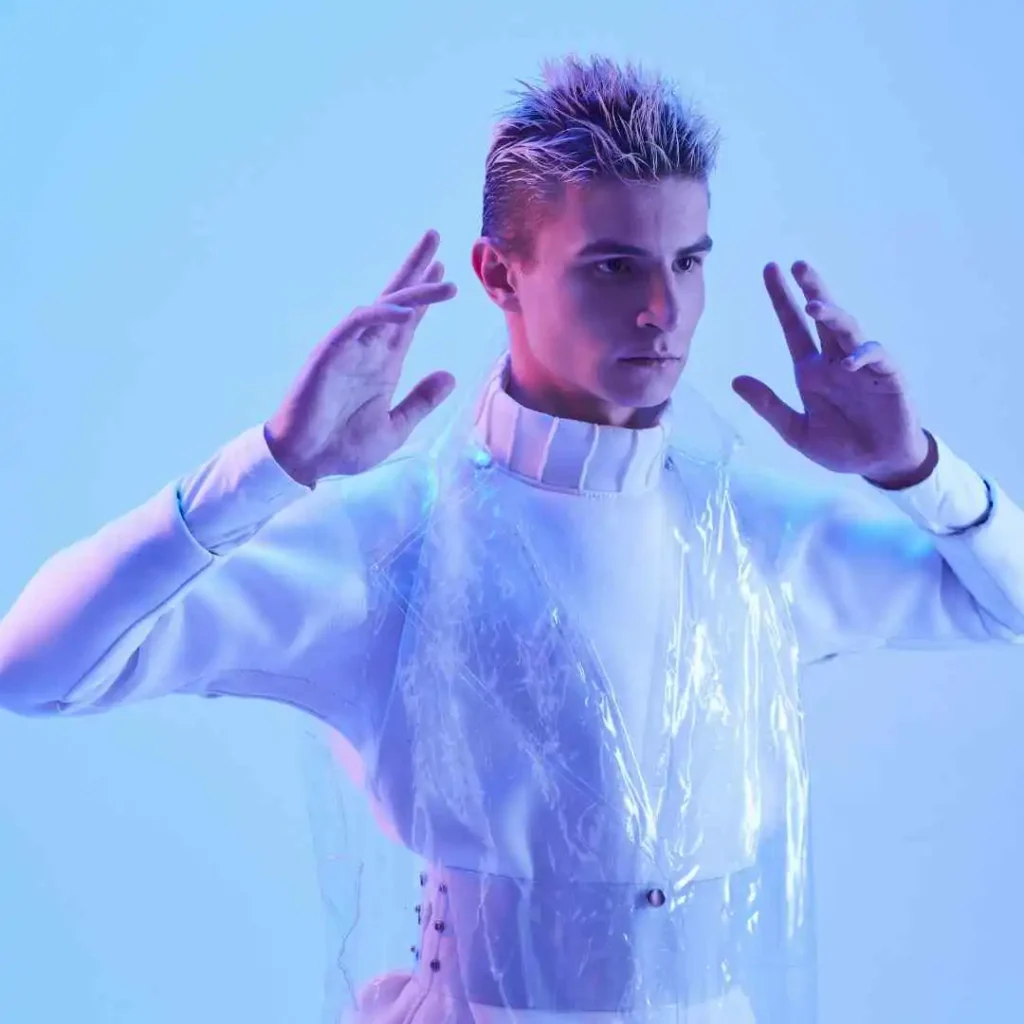 A person in a white shirt and translucent jacket with hands raised, under blue lighting, showing off a trendy summer hairstyles for men.