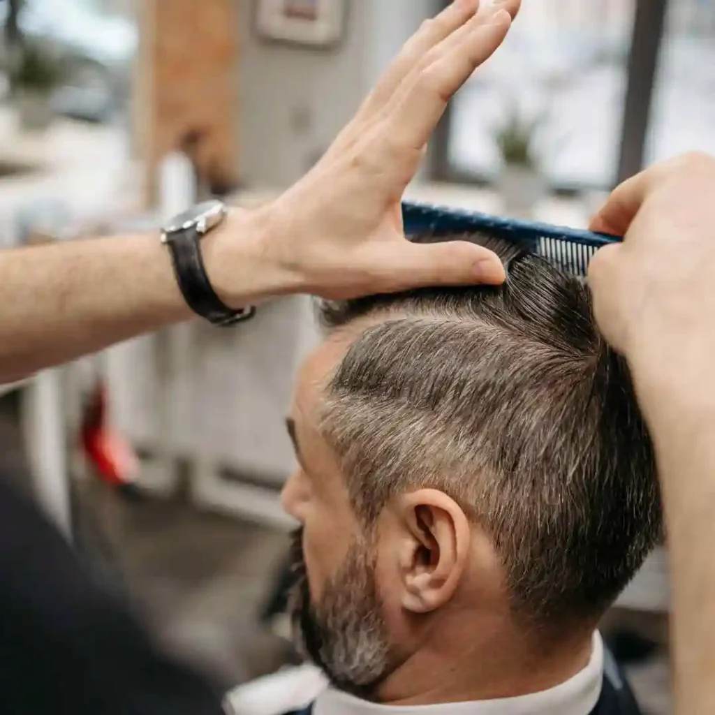 A barber expertly styles a client's hair using a blue comb, showcasing the precision of the haircut in a bright salon setting.