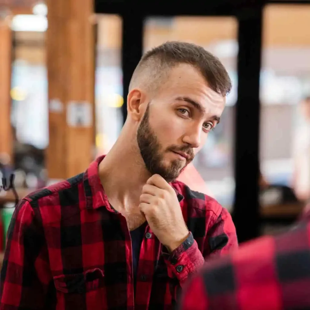 A person in a red and black plaid shirt looks pensive, holding their chin while mirrored reflections appear in the background.