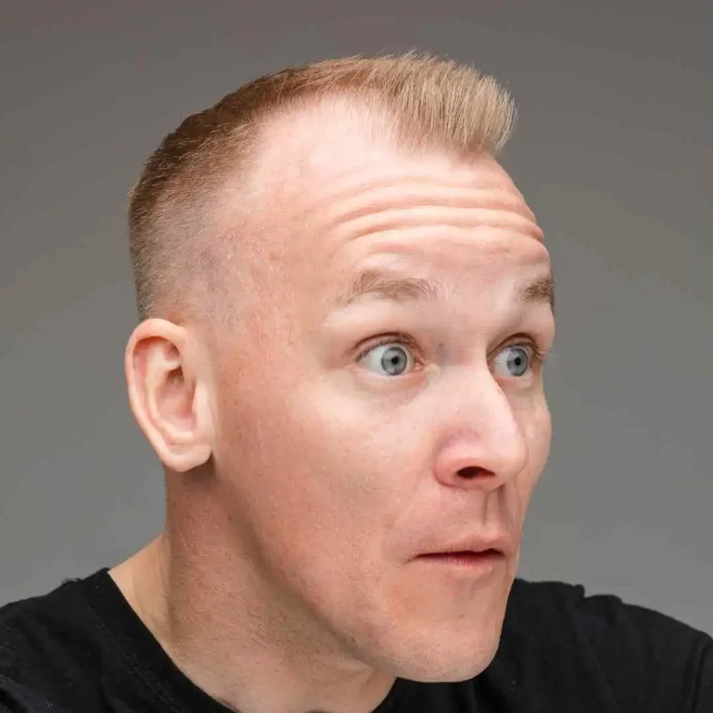 Modern Men Short Hairstyles- A Comprehensive Guide 4 Close-up of a person showcasing MODERN MEN SHORT HAIRSTYLES with short blonde hair, wearing a black t-shirt, against a soft gray background.