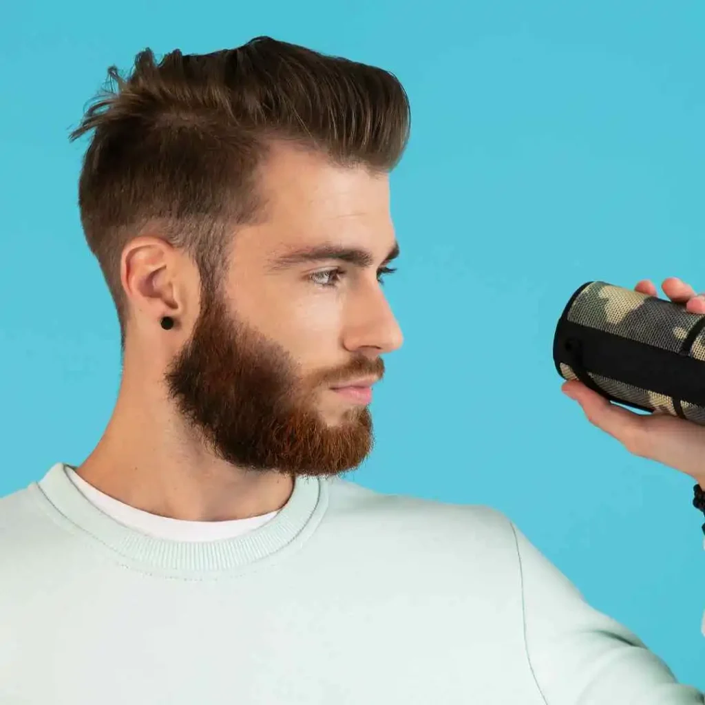 A person holds a stylish camo-patterned speaker in their right hand, set against a bright blue background.