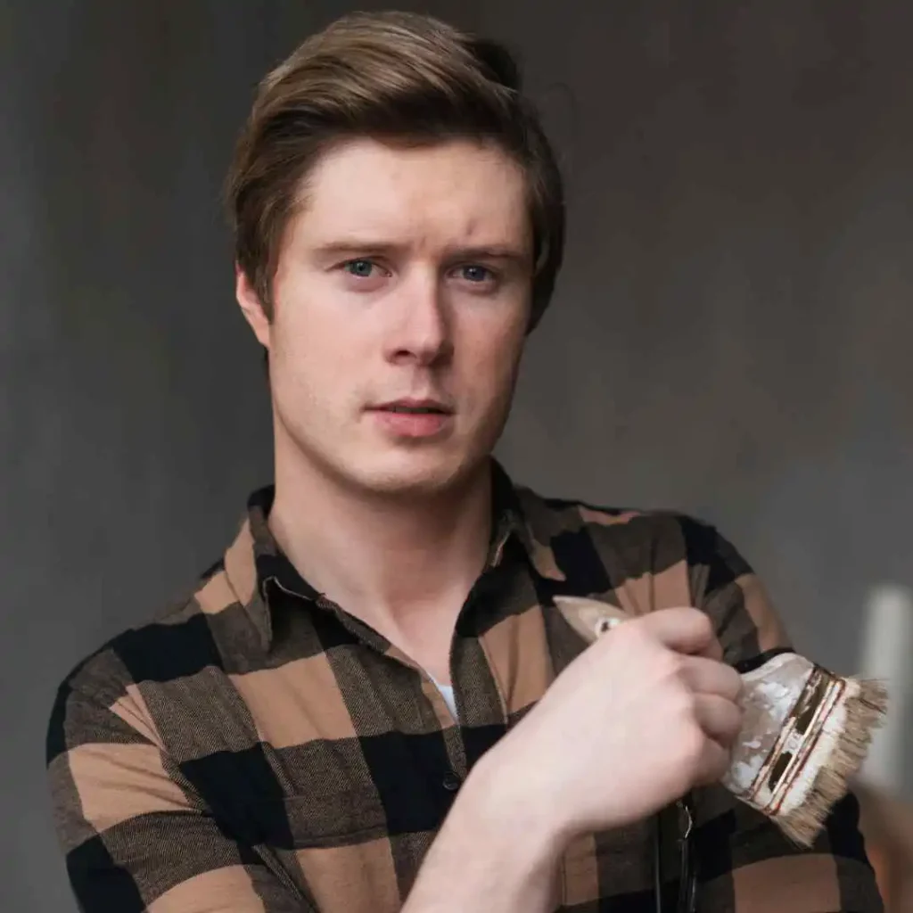 A person wearing a brown and black checkered shirt holds a paintbrush, showcasing creativity and readiness for a painting project.