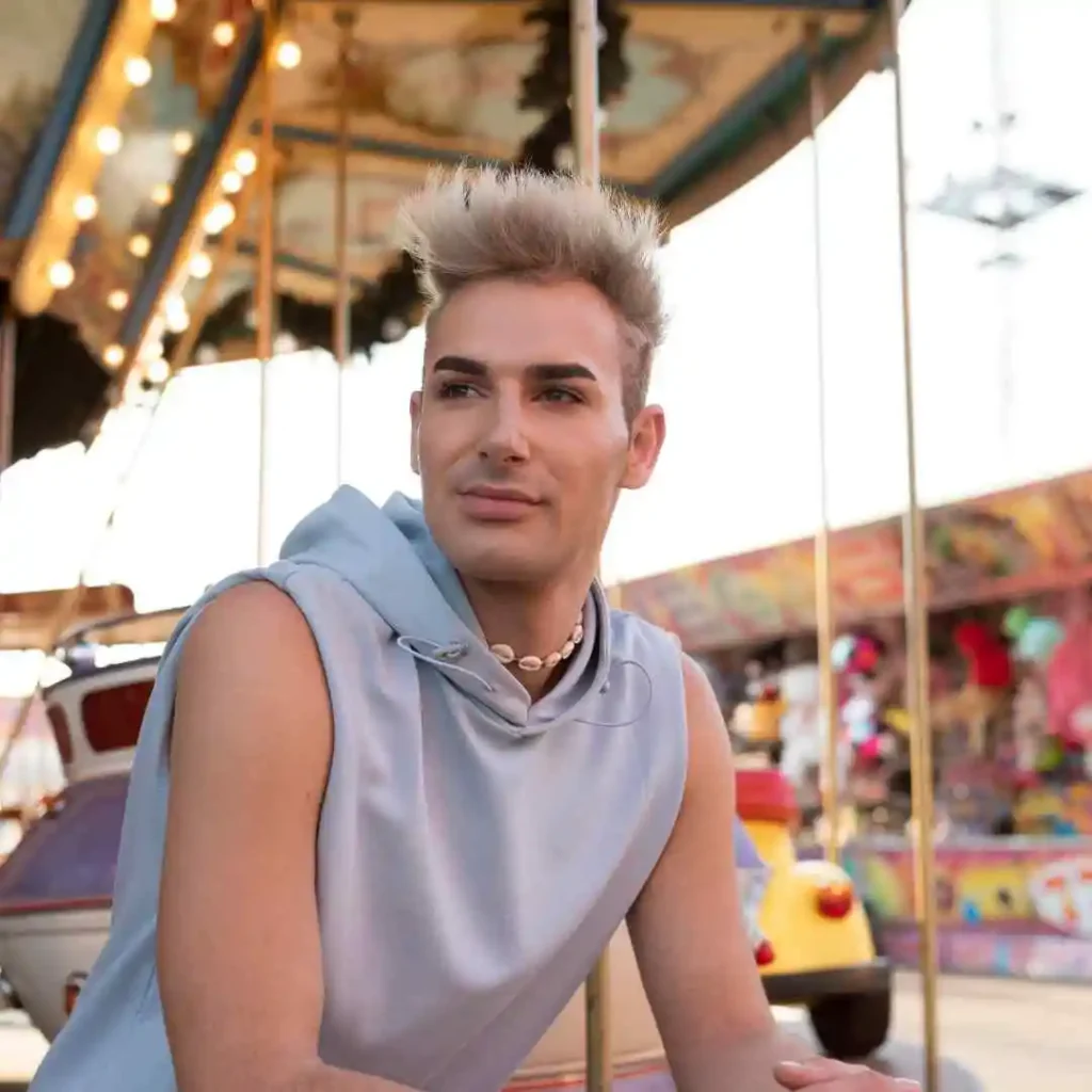 Discover 20 New Pompadour Hairstyles- A Comprehensive Guide 5 A person in a light blue sleeveless hoodie sits in front of a vibrant carousel, with colorful carnival rides in the background, showcasing pompadour hairstyles.