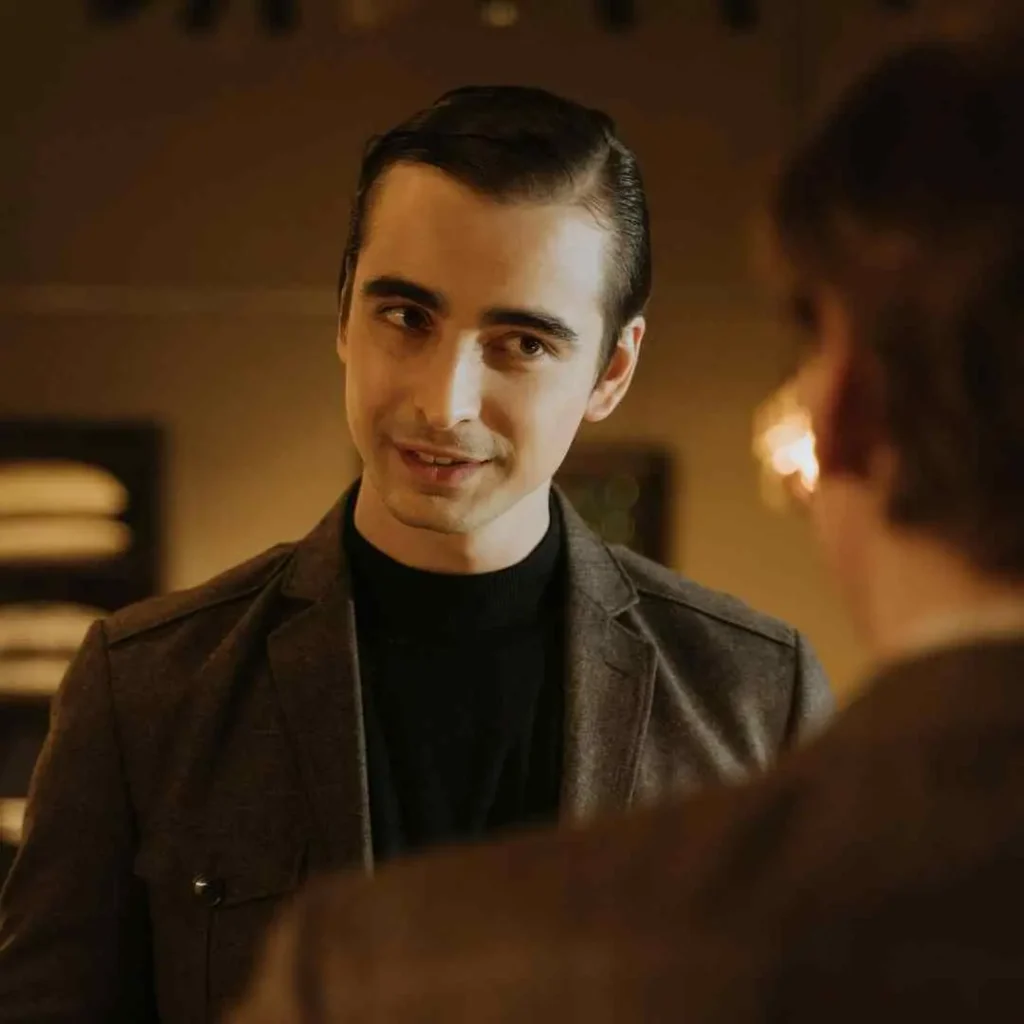 21 On-Trend Hairstyles for Men with Oval Face 5 A stylishly dressed man with a classic Men Hairstyles Oval Face look, wearing a brown blazer and black turtleneck, appears engaged in a serious conversation with another person.