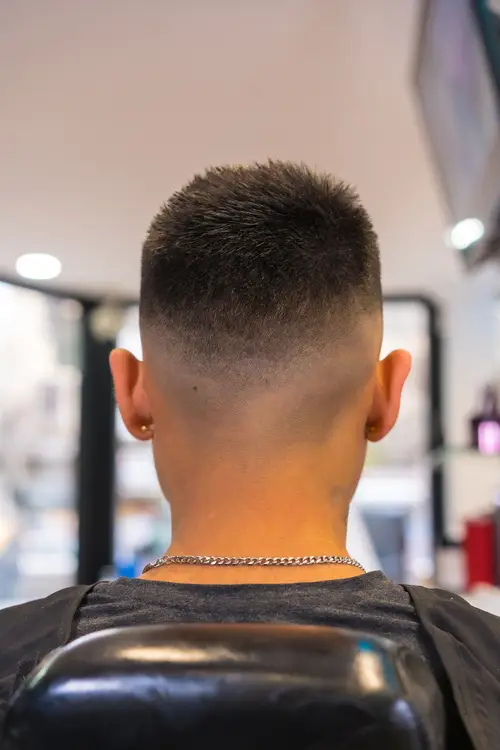 Top 15 Men Hairstyles for Buzz Cut 6 Close-up of a man's cropped, faded haircut from the back, showing a clean fade and short hair at the crown, in a barbershop setting.