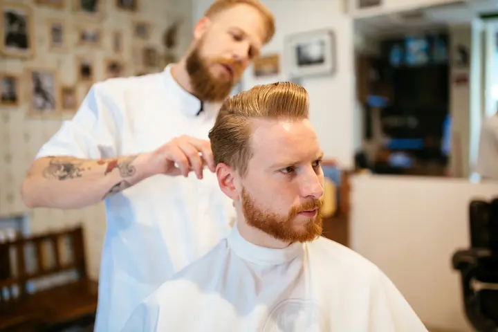 Discover 20 New Pompadour Hairstyles- A Comprehensive Guide 6 "A barber styles a client's hair in a modern barbershop, showcasing a relaxed atmosphere with wooden furniture and framed photos, while creating stylish pompadour hairstyles