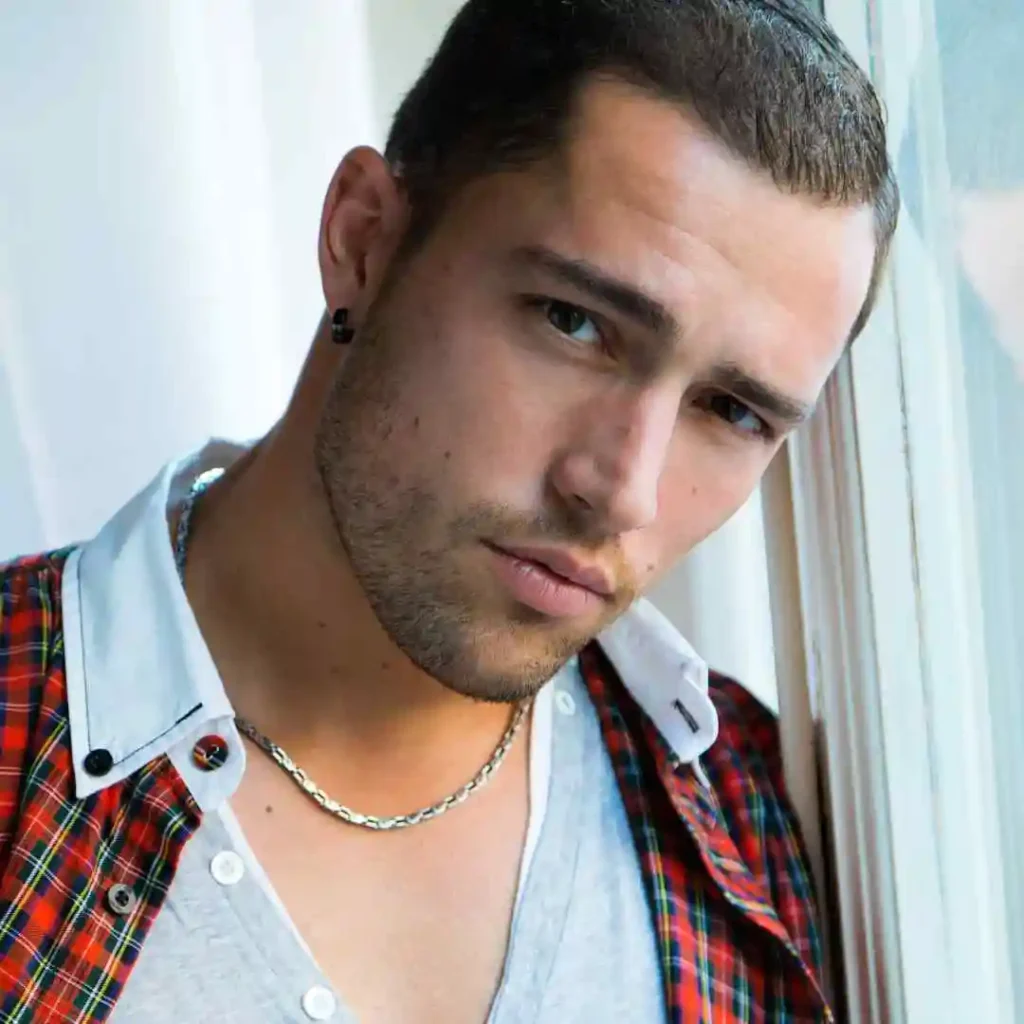 Top 15 Men Hairstyles for Buzz Cut 8 A person with a MEN HAIRSTYLES BUZZ CUT, wearing a casual outfit, leaning against a window with soft natural light illuminating the scene.