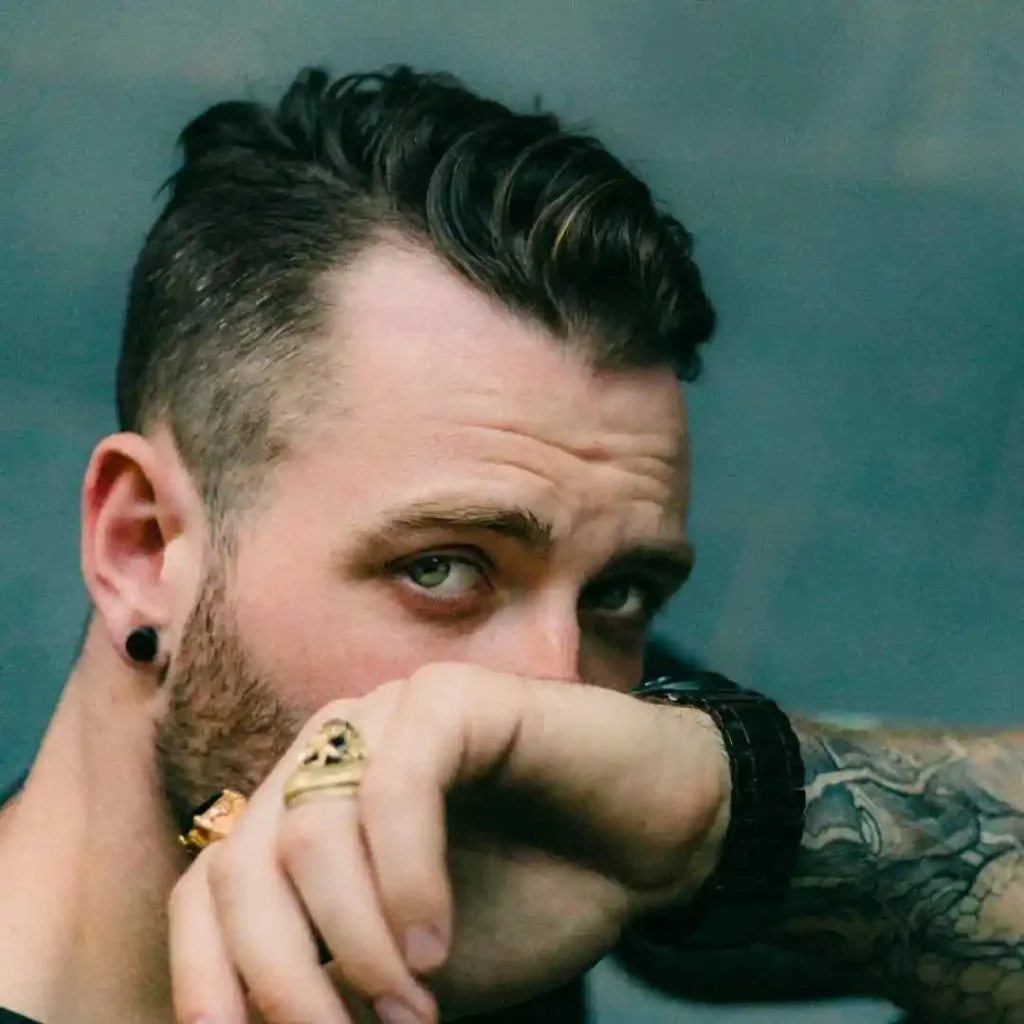 Person with a pompadour hairstyle and a tattooed arm wearing a black ear gauge.