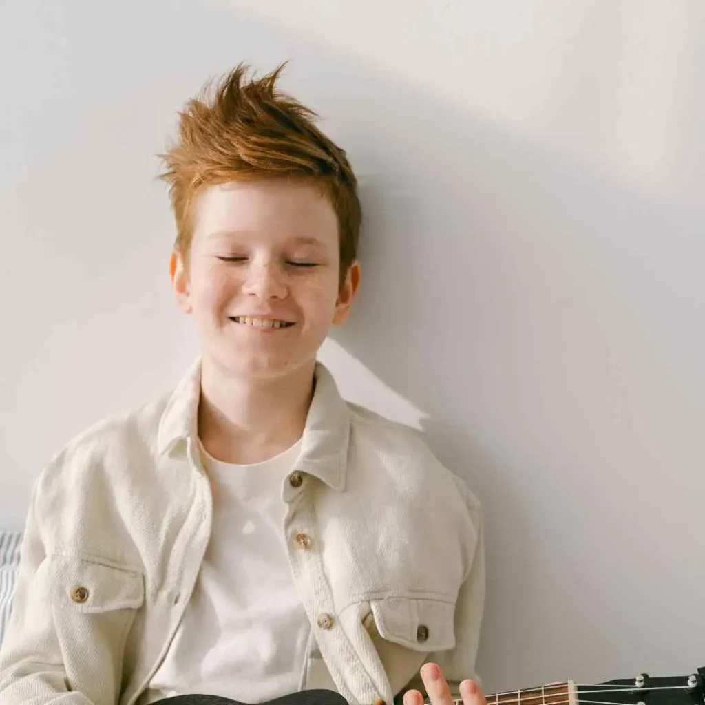 Person in a white jacket holding an acoustic guitar against a light background.