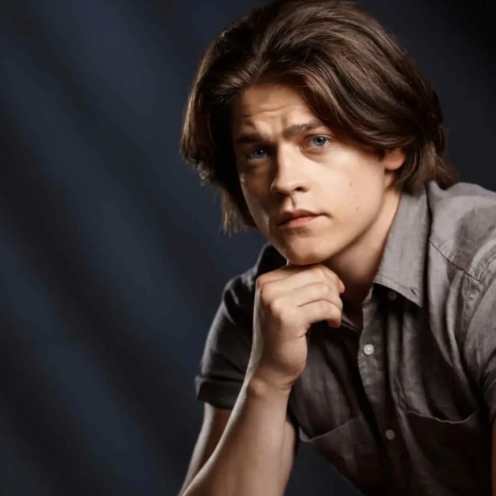 A person in a gray shirt thoughtfully rests their chin on their hand, set against a dramatic dark backdrop with soft lighting, showcasing men hairstyles curtains.