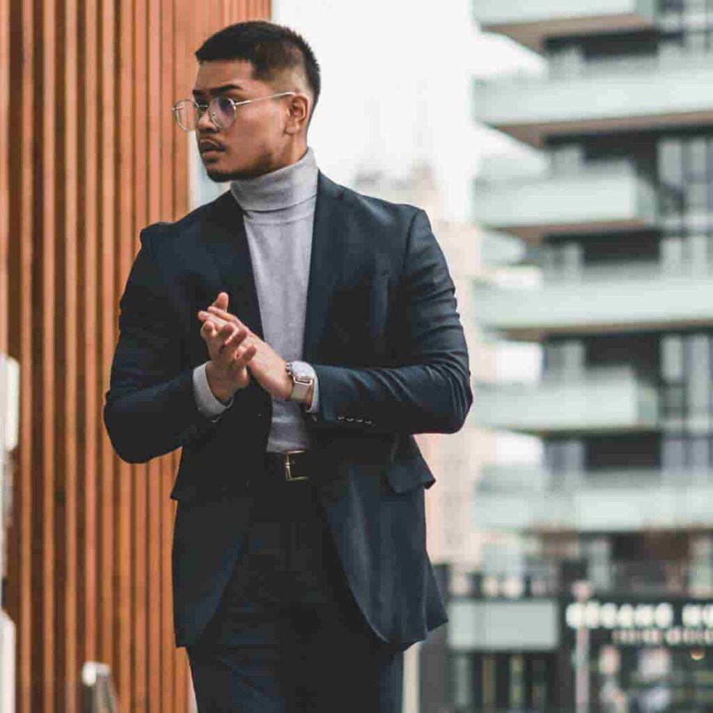 A man in a suit clapping his hands in an urban setting, sporting a clean men’s buzz cut hairstyles.