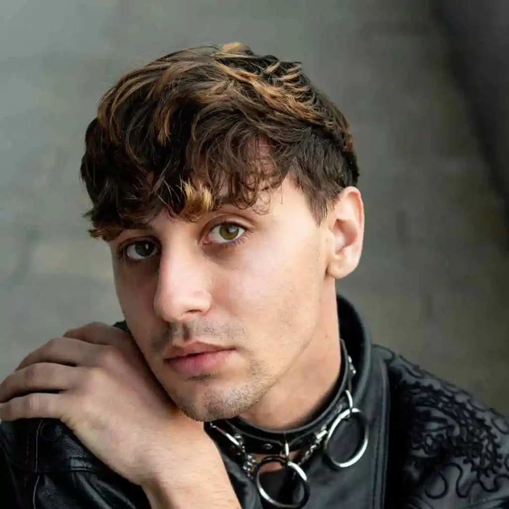 A young person with stylish, textured Edgar haircuts for men wears a black leather jacket and a silver chain necklace, resting a hand on their shoulder.