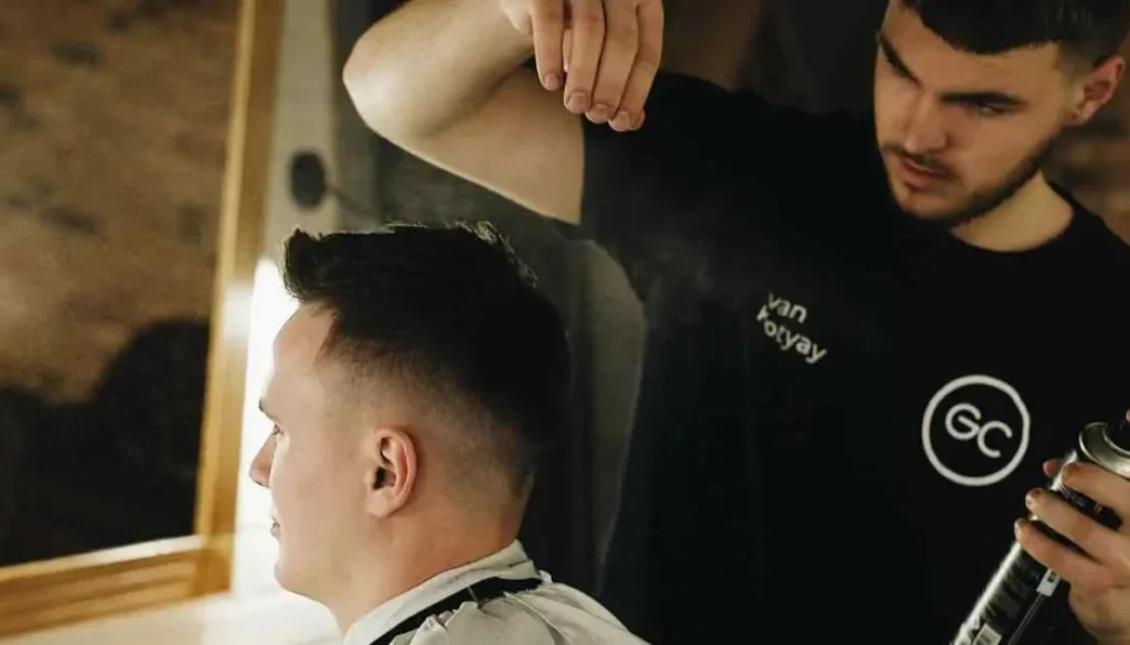 A hairstylist applying spray on a client's buzz cut in a salon, showcasing a popular men’s hairstyle.