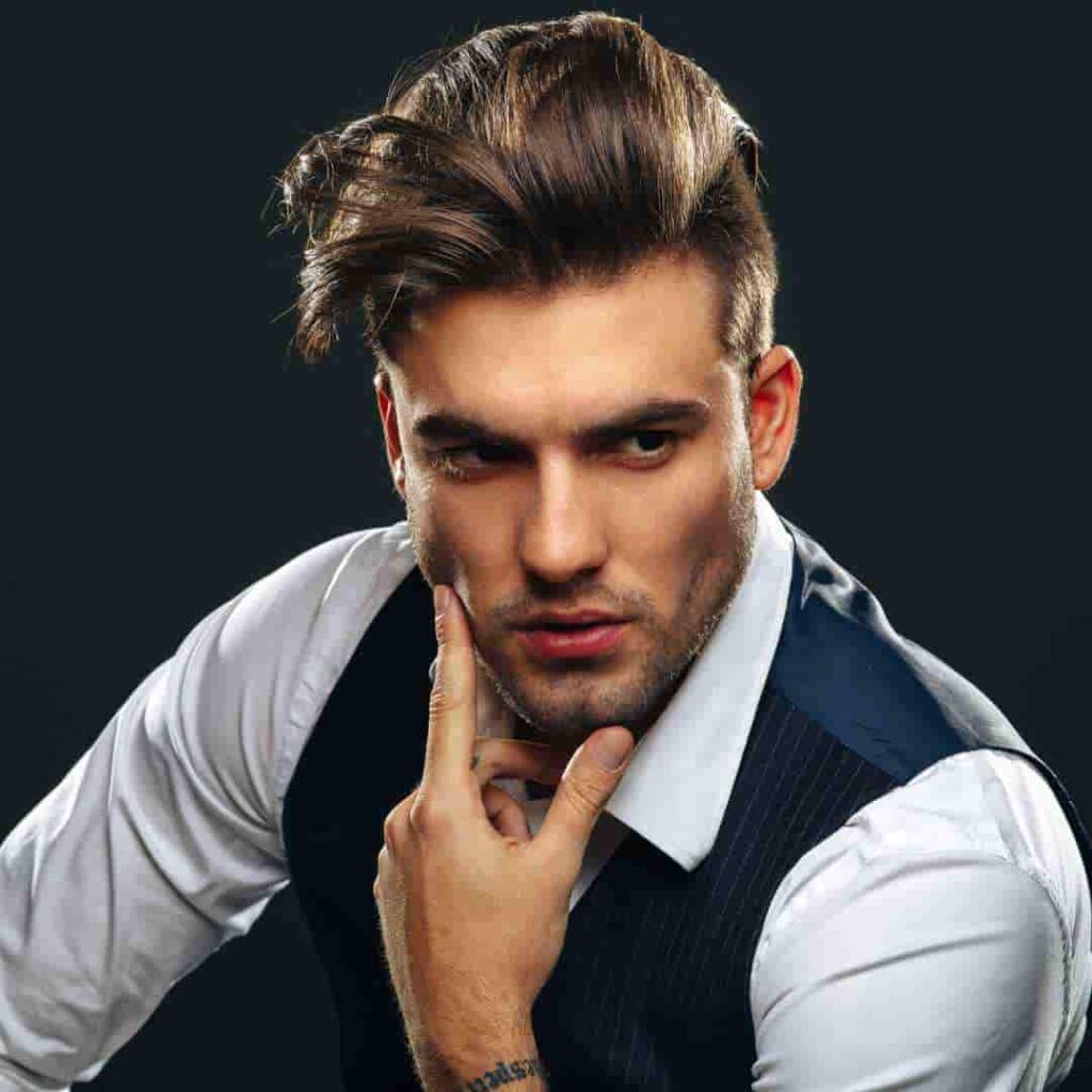 52 Mid-Length Hairstyles for Men- A Comprehensive Guide. 5 A stylishly dressed individual in a suit, posing with a thoughtful expression against a dark background.