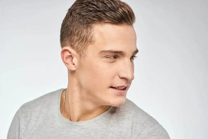 A young man with a FADE HAIRSTYLE FOR MEN, short and styled, wearing a gray t-shirt, looking slightly to the side against a light background.