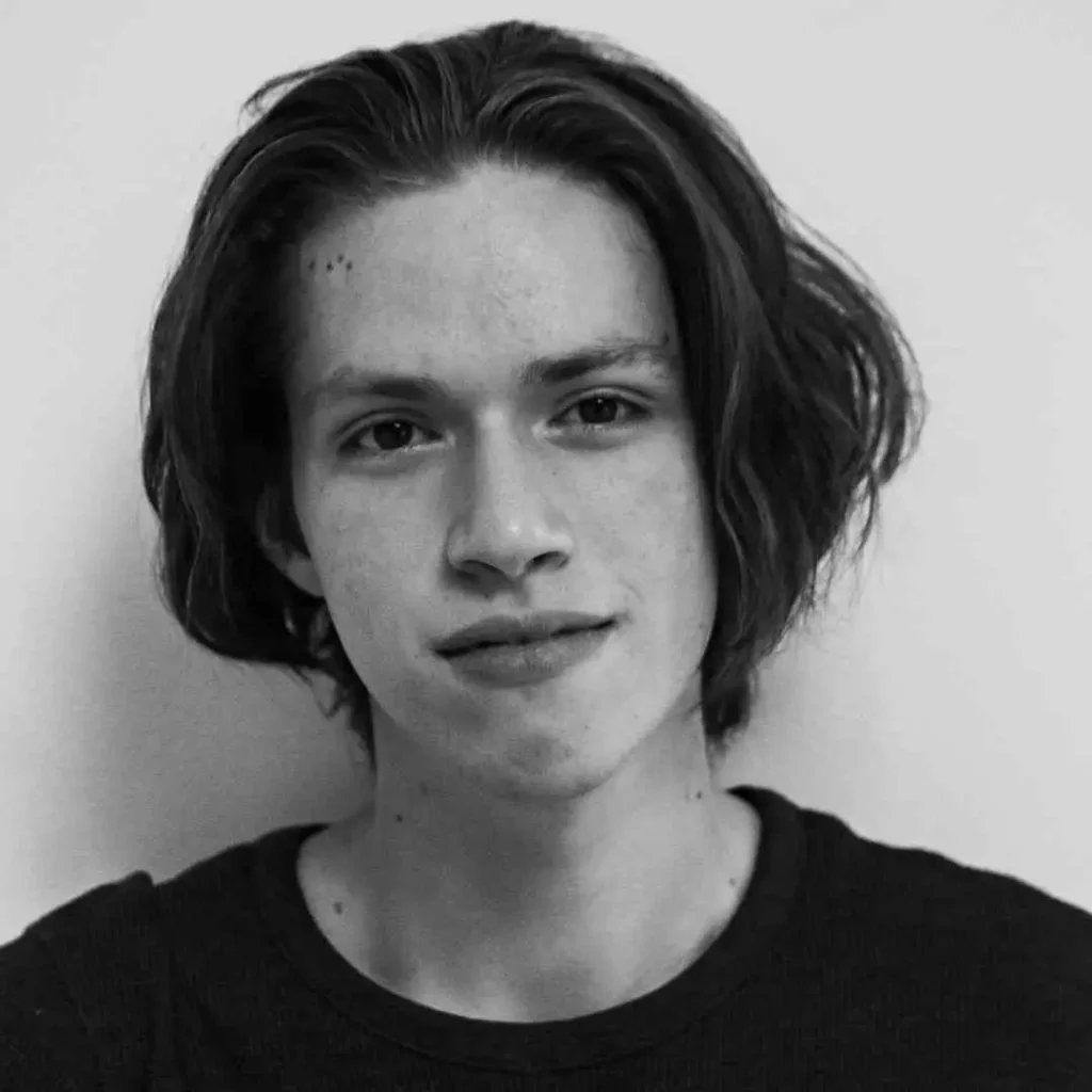 A person showcasing long hair styling for men with medium-length, wavy hair, wearing a black shirt, set against a plain white background.