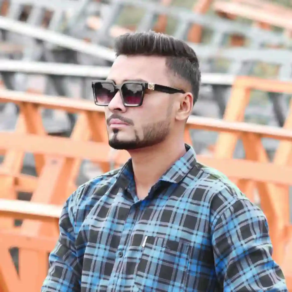 A person showcasing men hairstyles with glasses, wearing sunglasses and a blue plaid shirt, stands confidently against a backdrop of orange construction equipment.