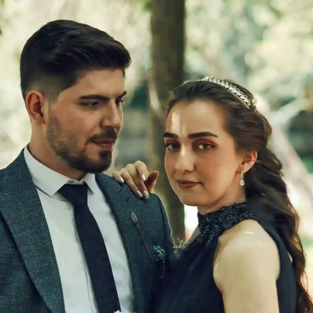 27 Wedding Hairstyles for Men That Can Elevate Your Style 2 A stylish couple poses together outdoors, showcasing elegant attire and a moment of intimacy amidst a natural backdrop, with the groom featuring a trendy wedding hairstyle for men