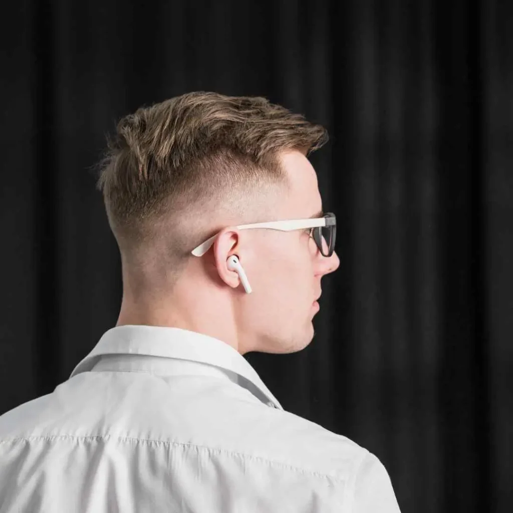 Cool And Breezy Summer Hairstyles for Men 4 A person showcasing one of the trendy summer hairstyles for men, with short, styled hair and wearing white wireless earbuds, seen from the back against a dark background.